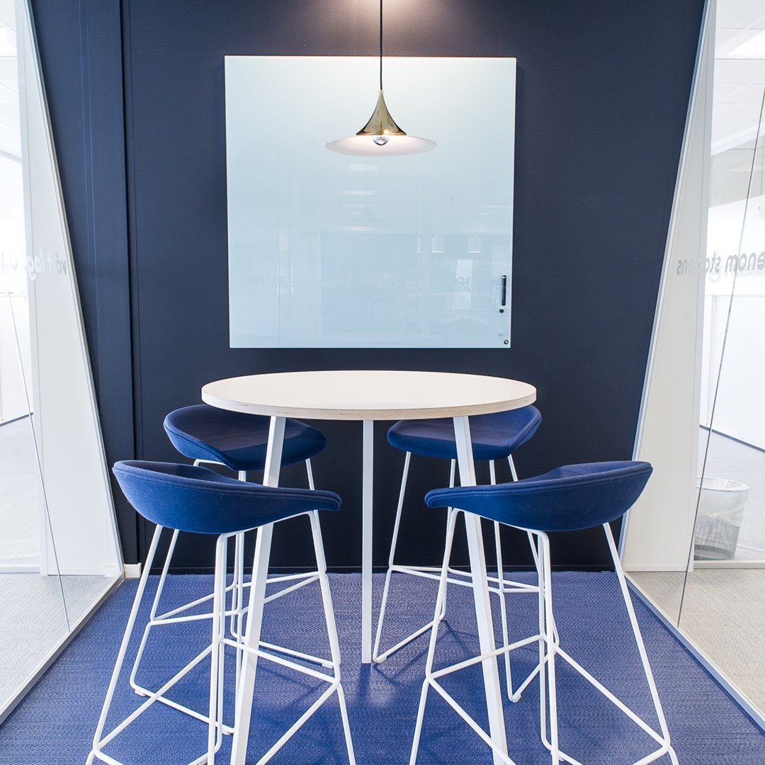 Round white table with blue upholstered stools on a dark blue background, featuring a minimalist pendant light.