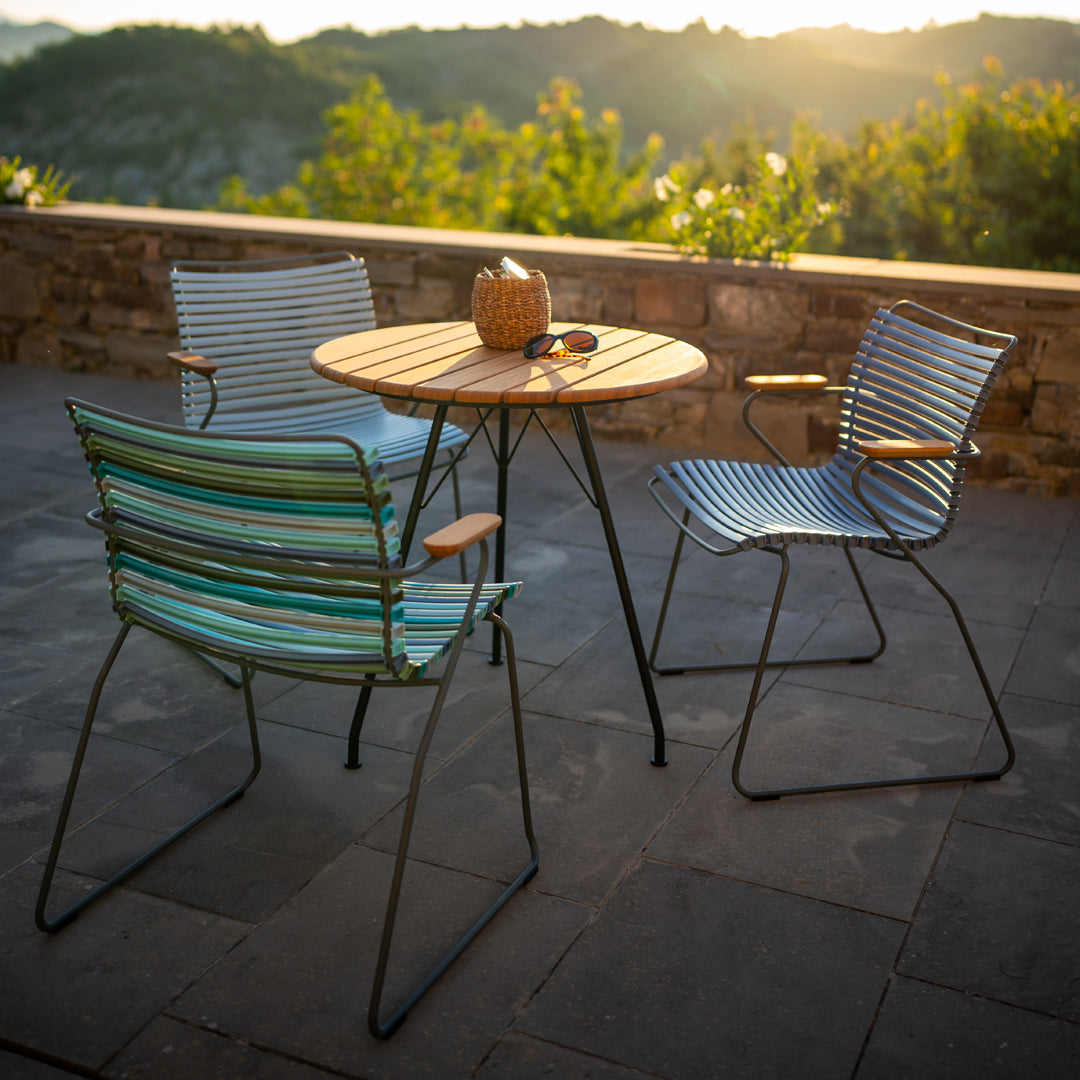 Colorful outdoor chairs with striped blue and green patterns and a rustic wooden table against a scenic backdrop.