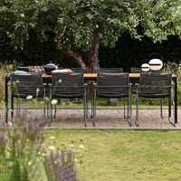 Black and gray striped chairs around a wooden dining table in a lush green garden setting.