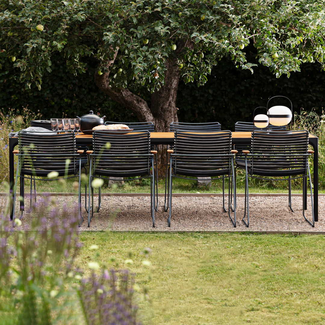 Black and gray striped chairs around a wooden dining table in a lush green garden setting.