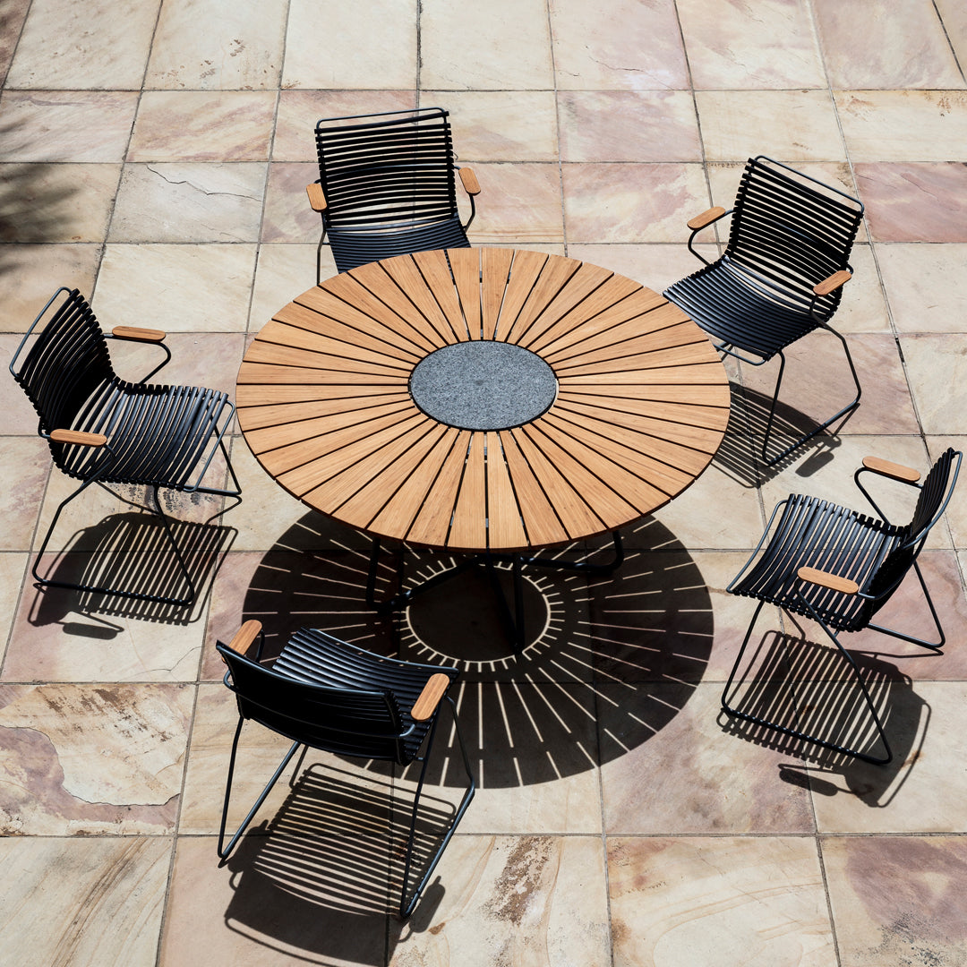 Round wooden dining table with a black metal chair surround, featuring a sunburst pattern on the tabletop.