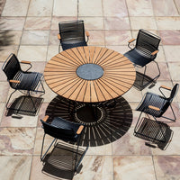 Round wooden dining table with a black metal chair surround, featuring a sunburst pattern on the tabletop.