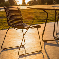 "Black metal chair with striped backrest, set against a sunlit patio and grass backdrop."