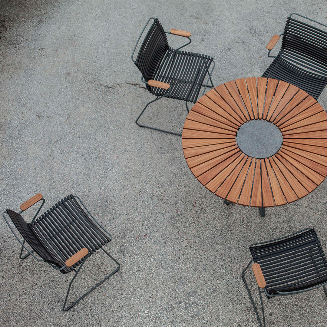 Black metal chairs with wooden armrests around a round wooden slat table. Elegantly modern outdoor dining set.