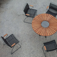Black metal chairs with wooden armrests around a round wooden slat table. Elegantly modern outdoor dining set.