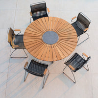 Round wooden dining table with gray center, surrounded by black striped chairs. Elegant outdoor seating design.