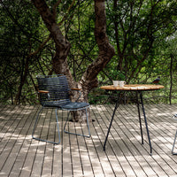 "Stylish blue striped chair beside a natural wood table with a dark metal base, set on a wood deck amidst greenery."