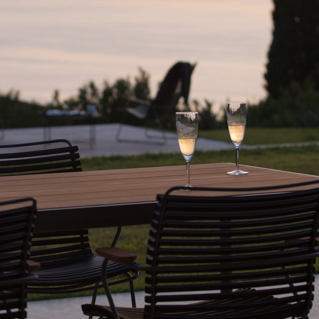 Elegant black outdoor chairs with a wooden table and clear champagne glasses against a soft sunset backdrop.