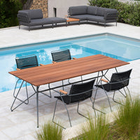 "Elegant outdoor dining set featuring a wooden table with a slatted design and black striped chairs by a poolside."