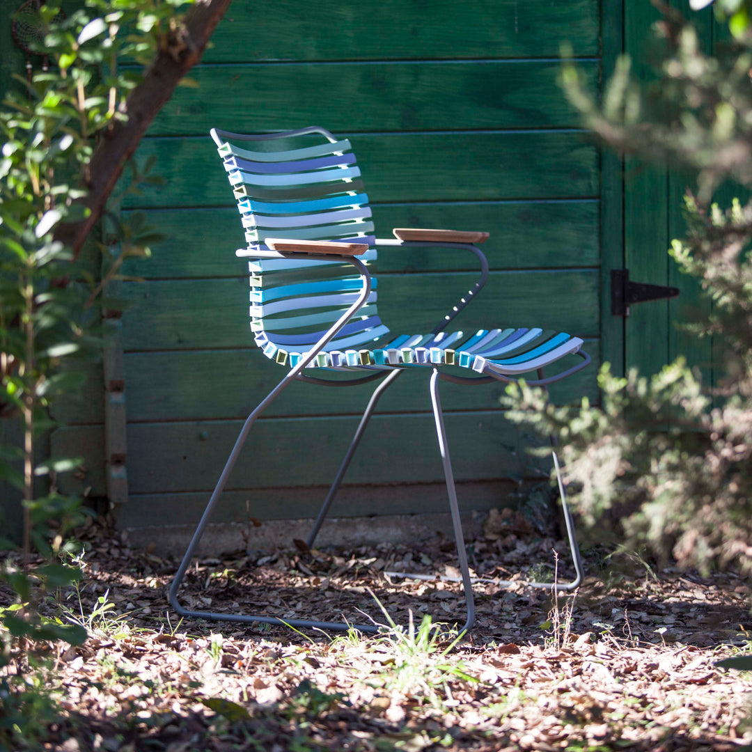Blue and green striped chair with wooden armrests, set against a rustic green backdrop. Ideal for outdoor decor.
