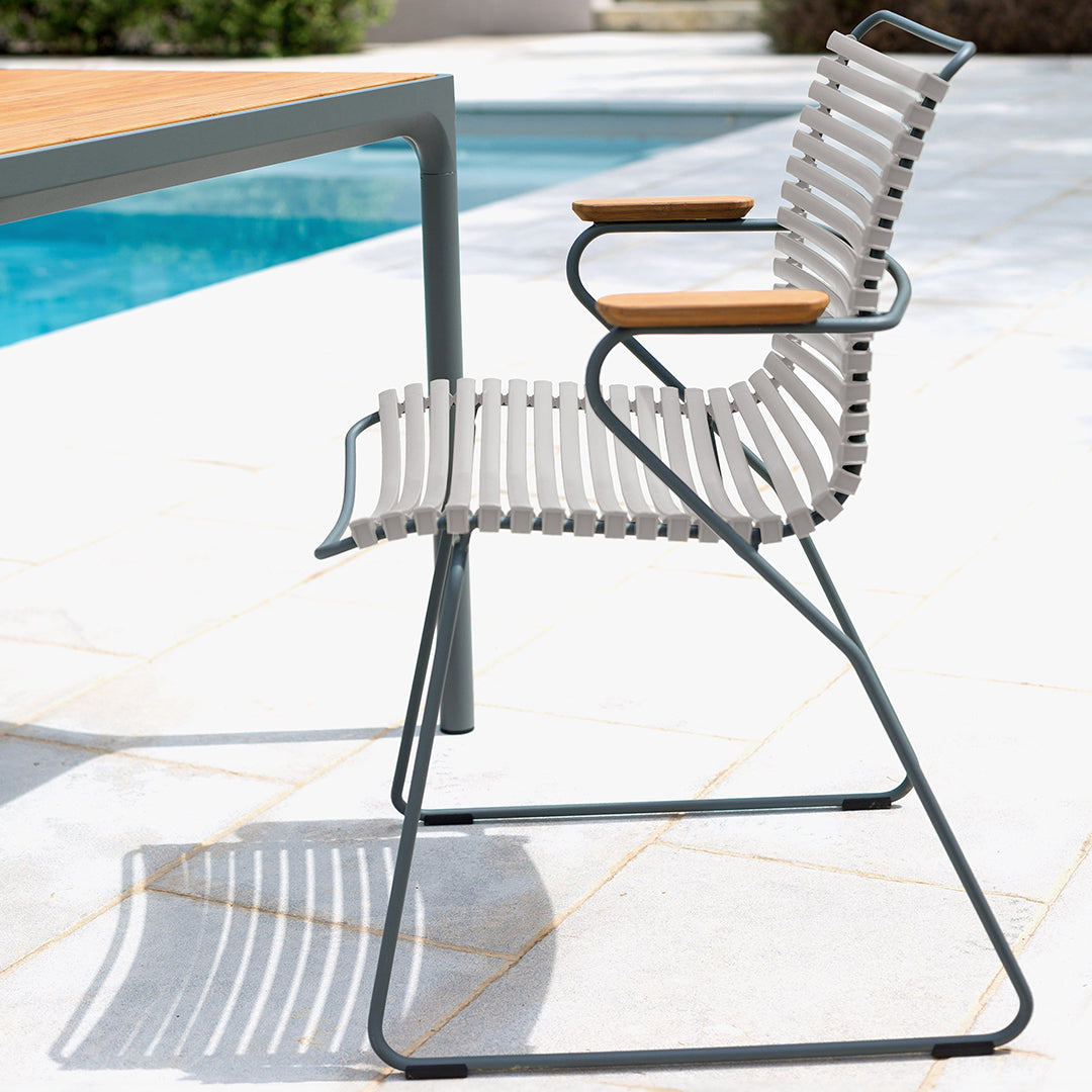 Gray and white striped outdoor chair with natural wood armrests, set near a pool on a tile patio.