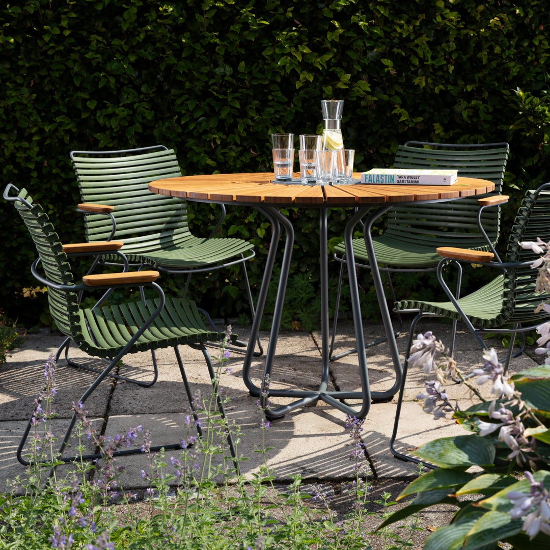 Green striped chairs paired with a round wooden table, set against lush greenery and vibrant flowers.