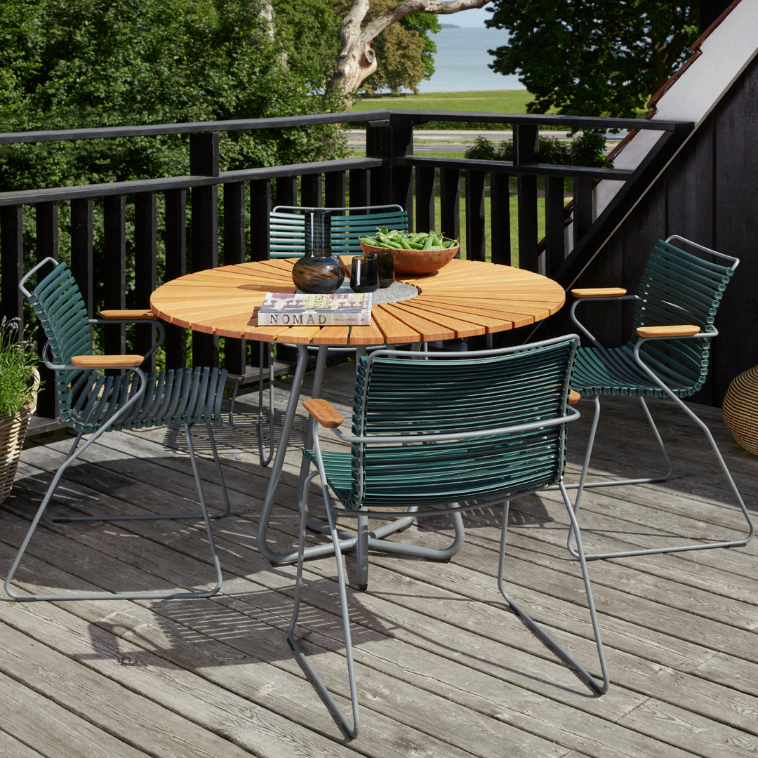 Round wooden table with green woven chairs, featuring gray metal frames on a wooden deck. Perfect for outdoor dining.