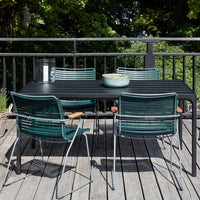 "Black outdoor table with teal striped chairs, surrounded by greenery and sunlight."