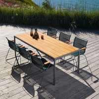 "Modern outdoor dining set featuring a light wooden tabletop and dark green striped chairs against a scenic backdrop."