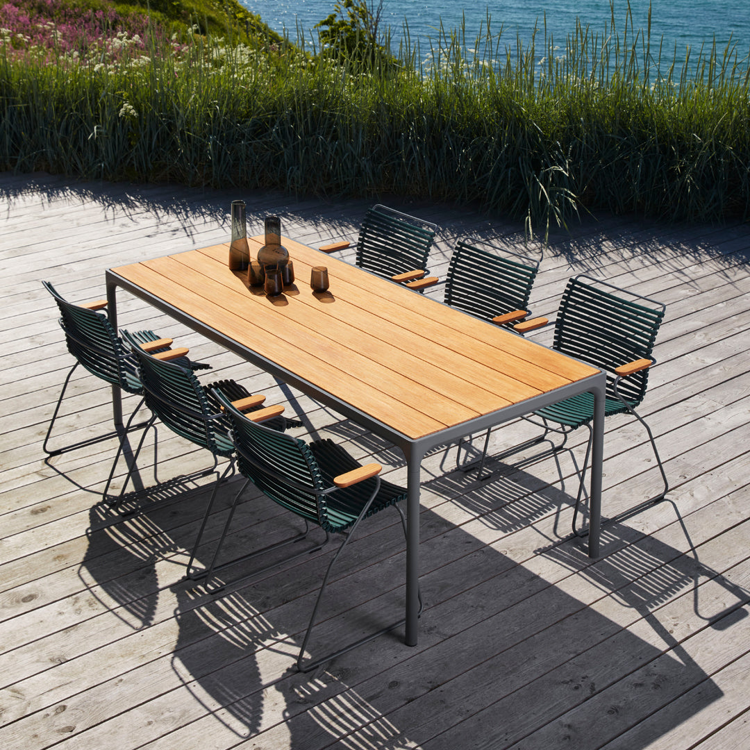 "Modern outdoor dining set featuring a light wooden tabletop and dark green striped chairs against a scenic backdrop."
