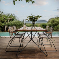 Brown wooden table with black metal frame and striped chairs, set against a green landscape under a blue sky.