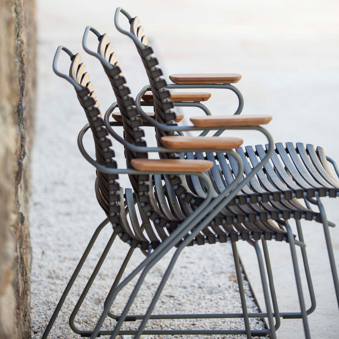 Stacked outdoor chairs in dark gray with natural wood accents, featuring a sleek, modern design and curved patterns.