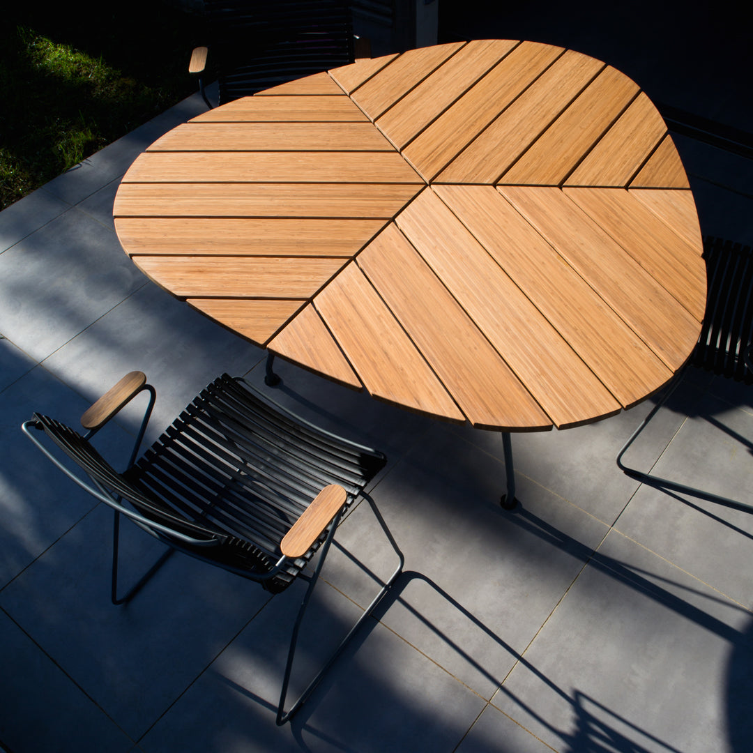 Stylish wooden table with a unique leaf pattern, complemented by sleek black chairs, set against a grey tiled surface.