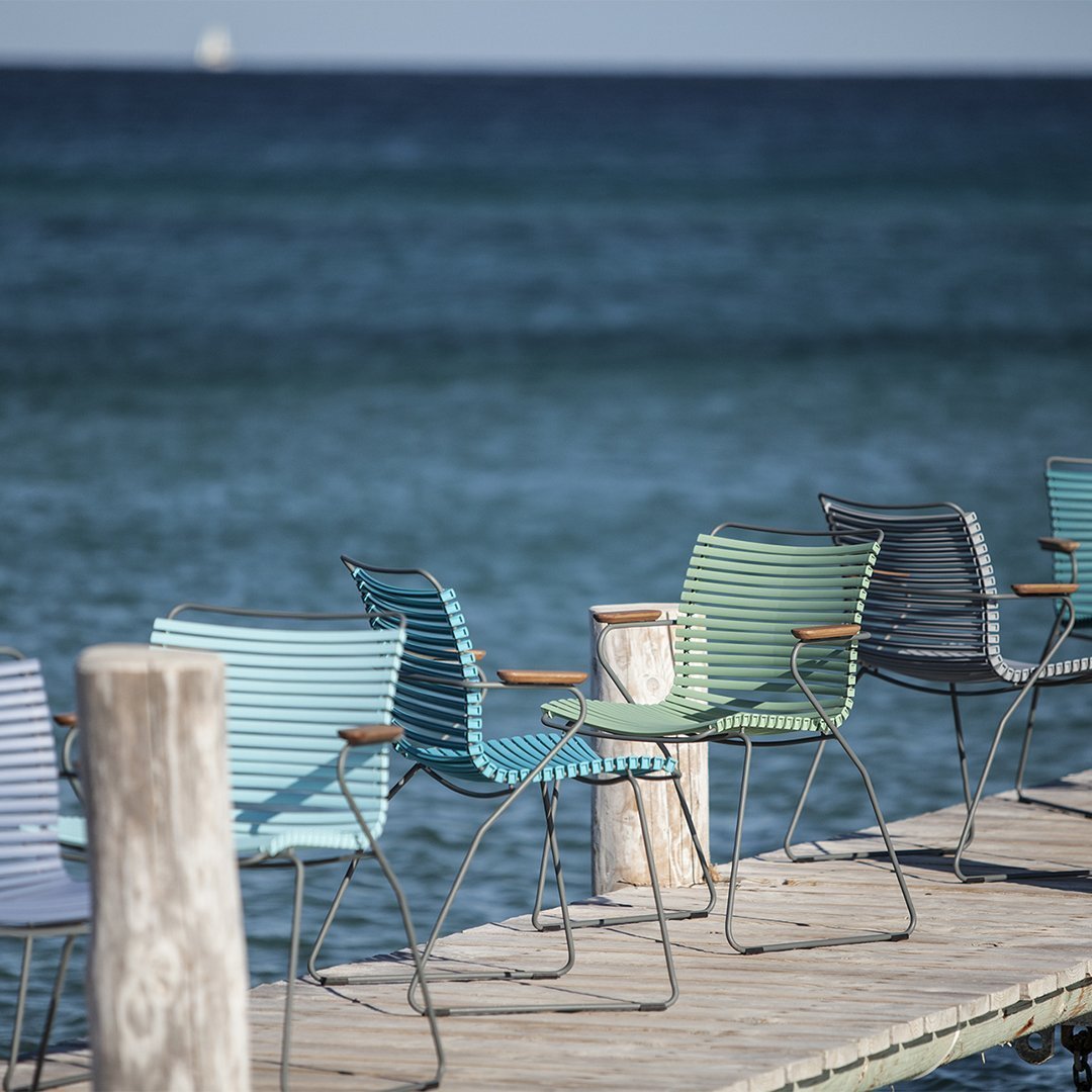 Colorful striped chairs in shades of blue, green, and gray lined up on a wooden dock by the sea.