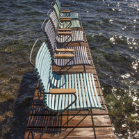 "Set of striped teal and white lounge chairs with wooden armrests on a wooden dock by sparkling water."