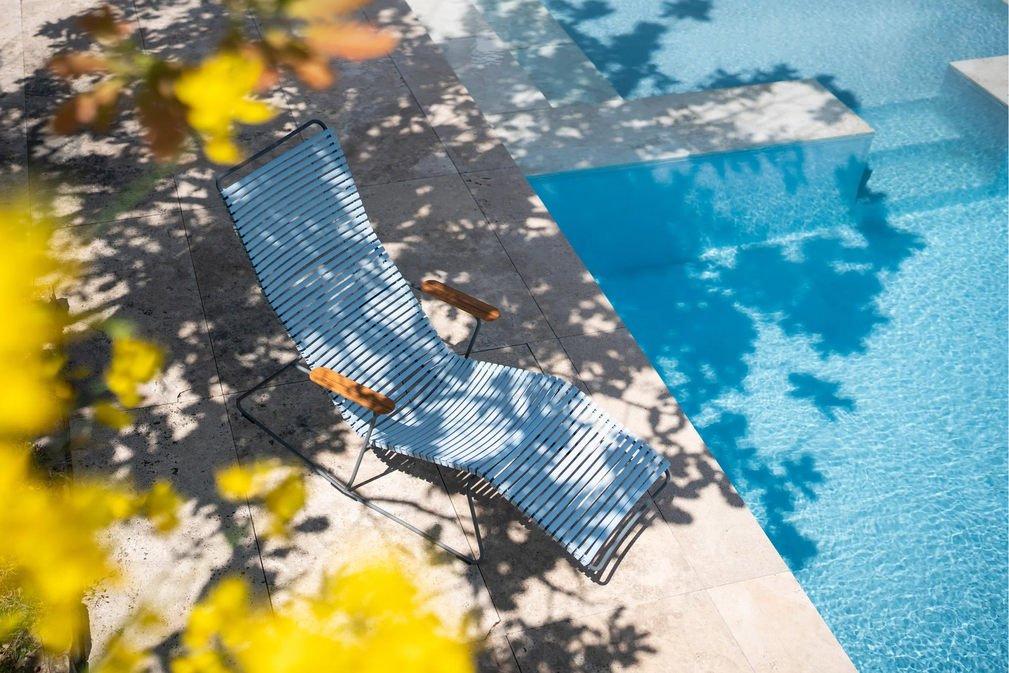 Blue lounge chair by a pool with yellow flowers in the foreground
