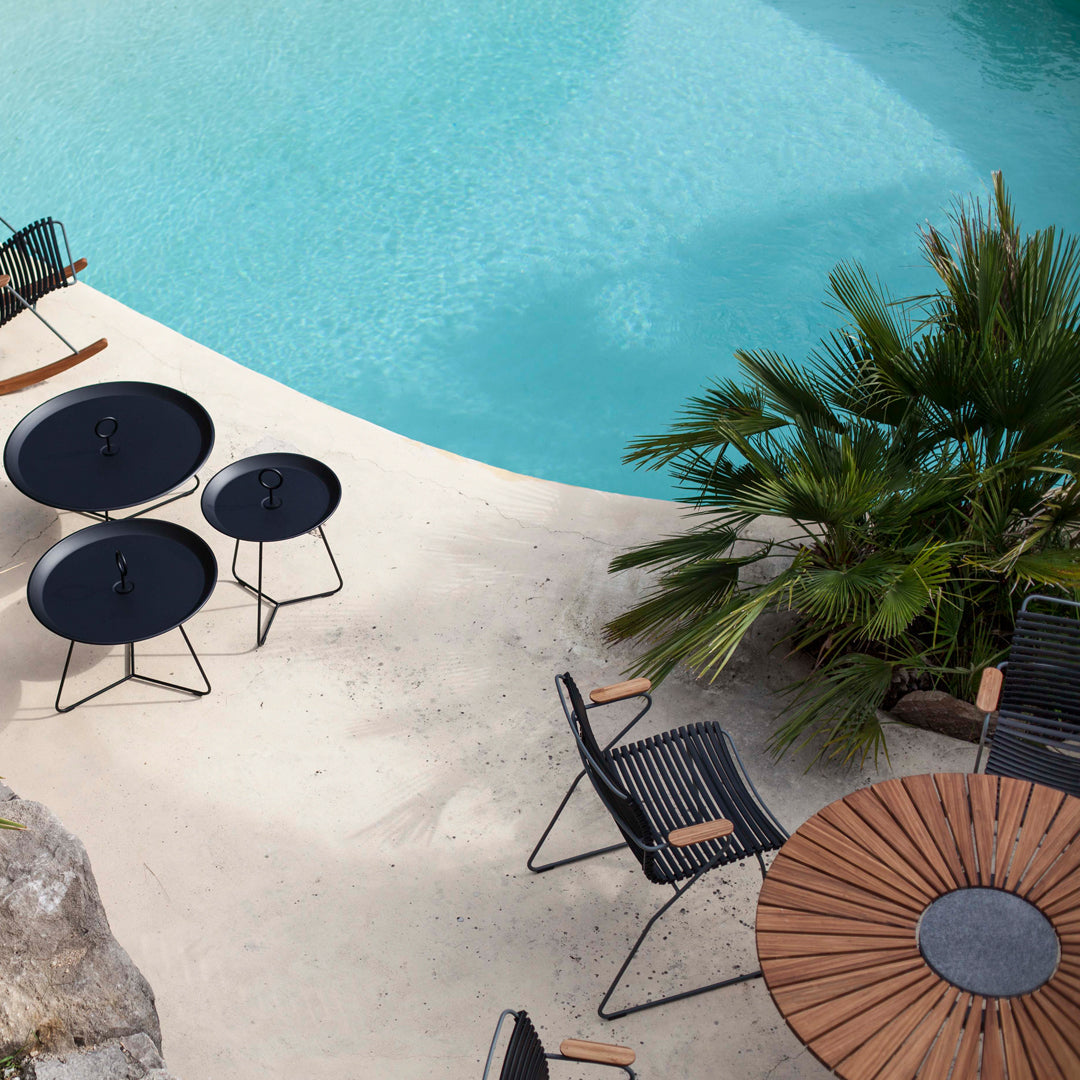 Outdoor seating set featuring black tables and striped chairs, set against a turquoise pool and green palm backdrop.