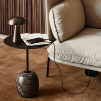 Stylish black side table with a smooth circular top, featuring a marble base, set against a soft beige fabric sofa.