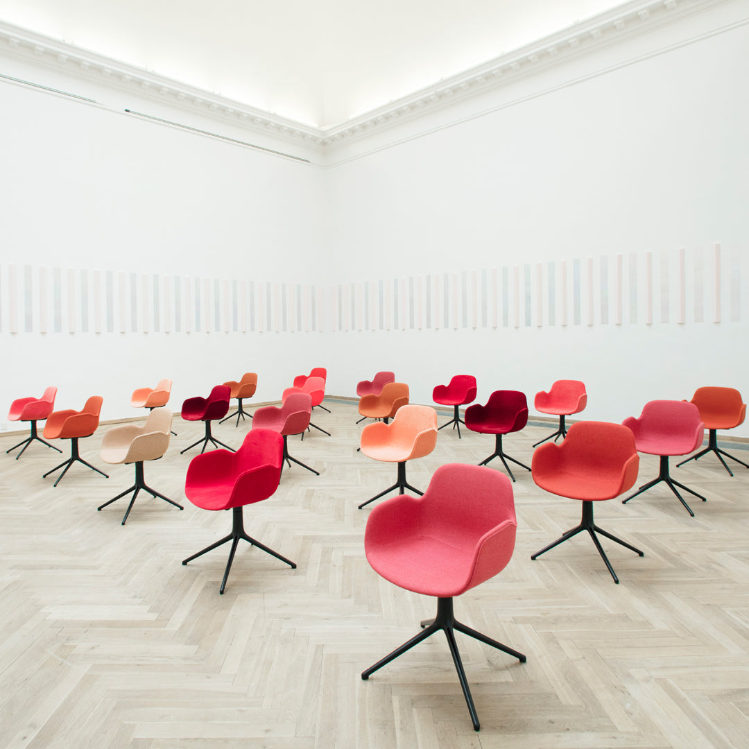 Colorful modern chairs in shades of red, orange, and peach set against a bright, minimalist backdrop.