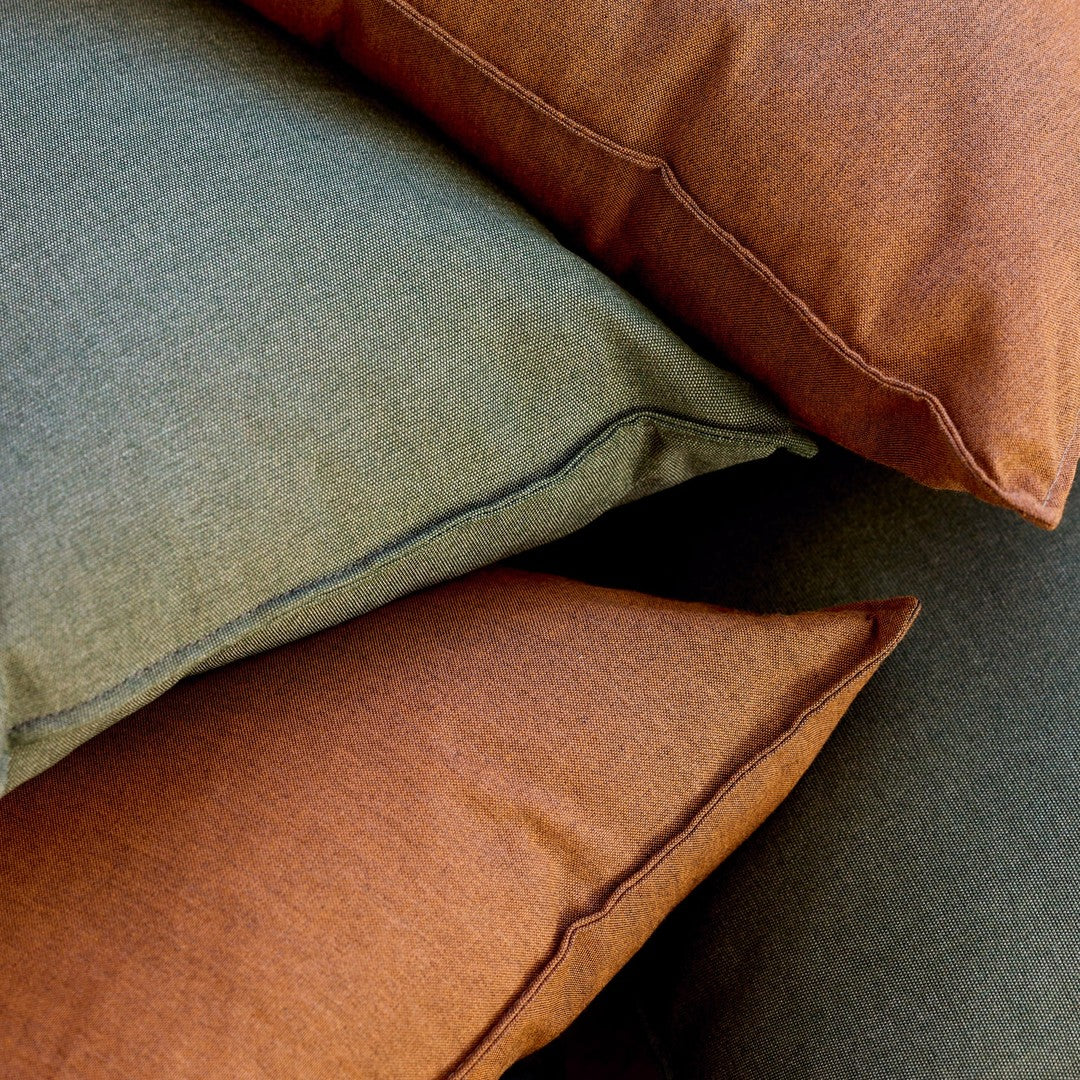 Stack of textured throw pillows in olive green and burnt orange, featuring subtle patterns and contrasting edges.