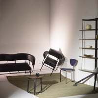 Sleek black furniture with geometric design on a neutral rug, accented by a purple chair against a minimalist backdrop.