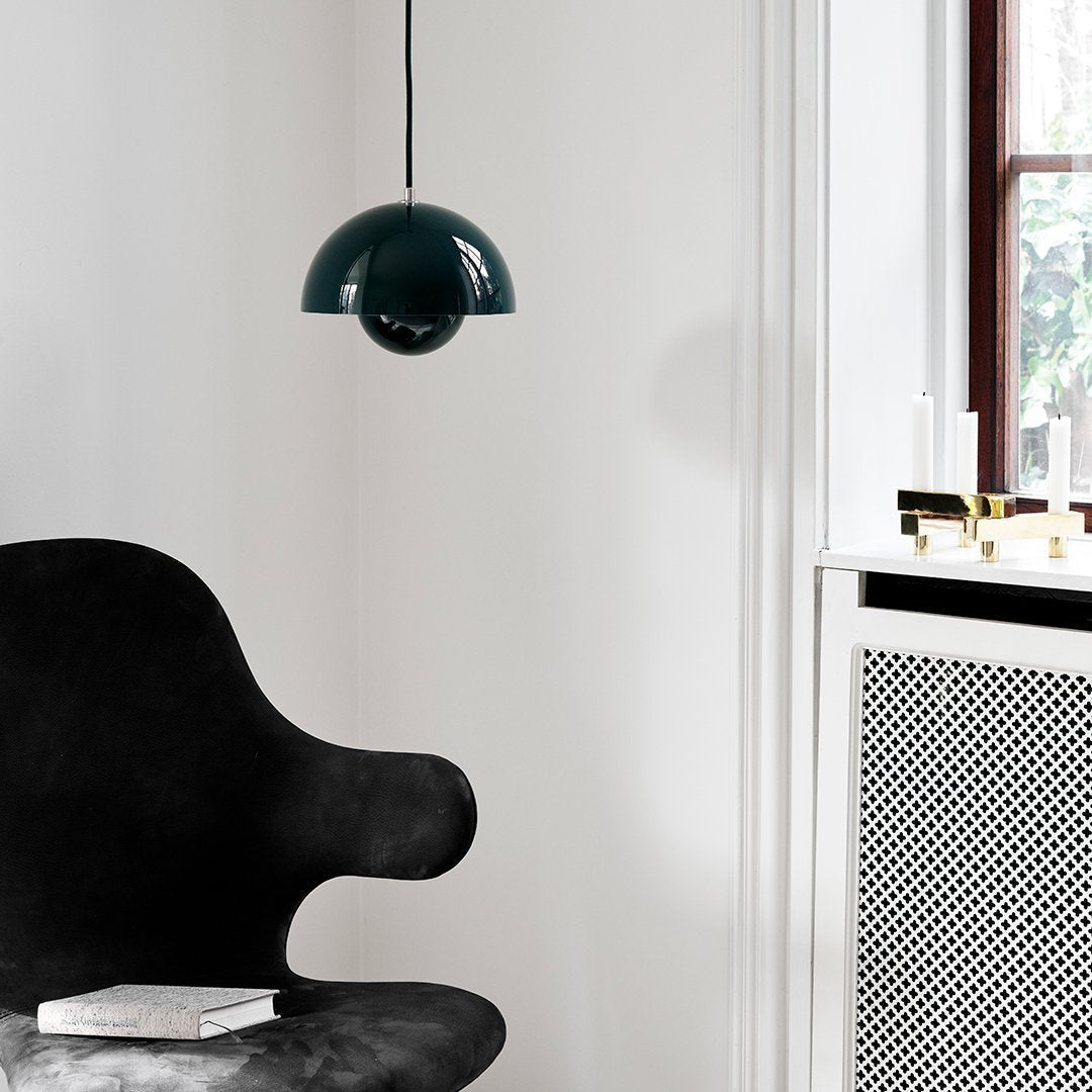 Glossy dark green pendant light hanging above a sleek black chair, against a minimalist white wall with a patterned radiator.
