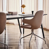 Tan upholstered chair with a sleek silver base, set against a warm wood floor and soft beige curtains.