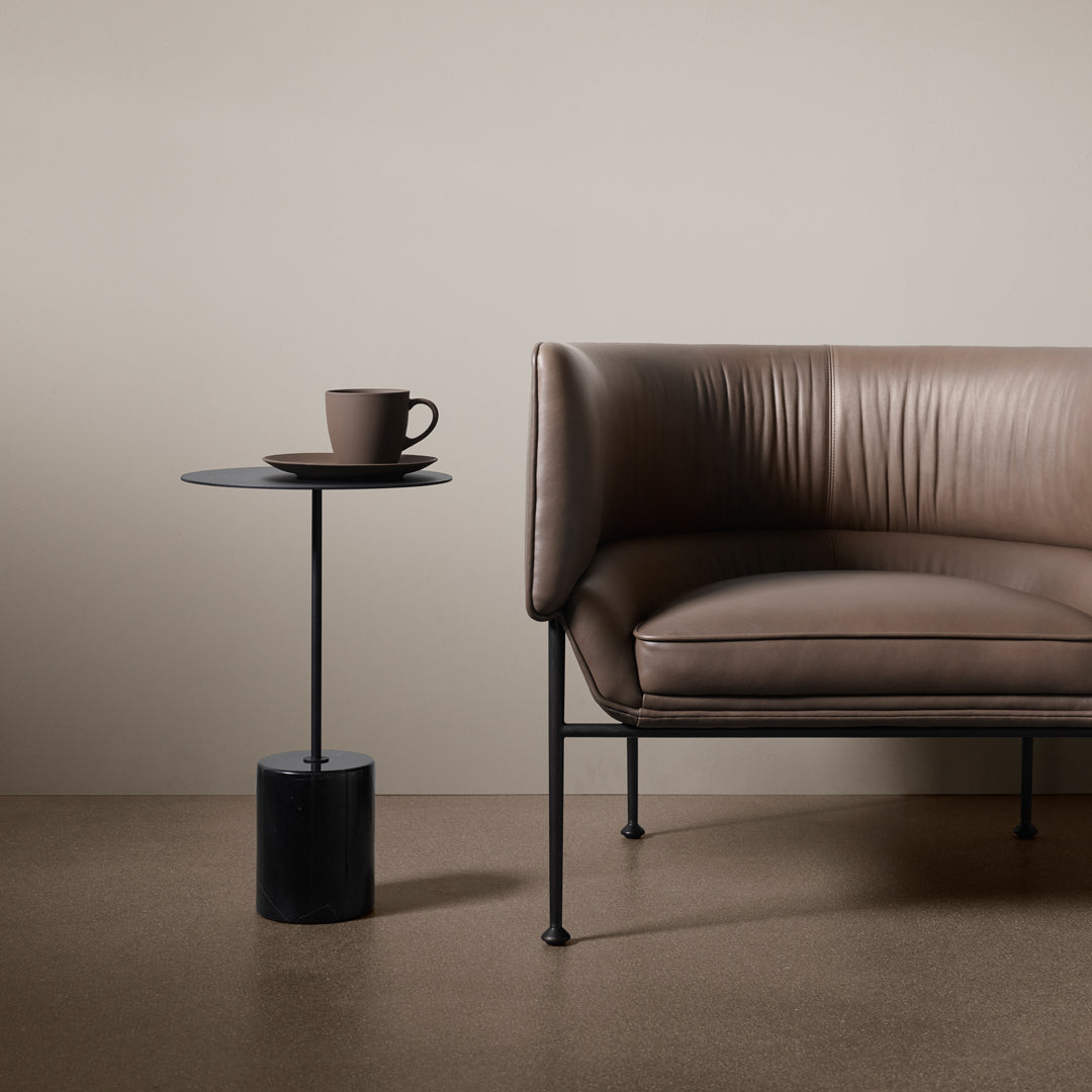 Brown leather sofa with horizontal ribbed texture, paired with a sleek black side table and a coffee cup.