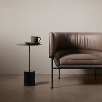 Brown leather sofa with horizontal ribbed texture, paired with a sleek black side table and a coffee cup.