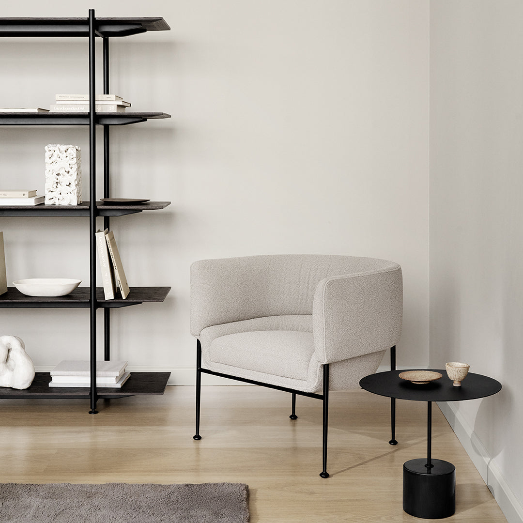 Cozy light gray upholstered chair with black metal legs, paired with a sleek black side table in a minimalist setting.