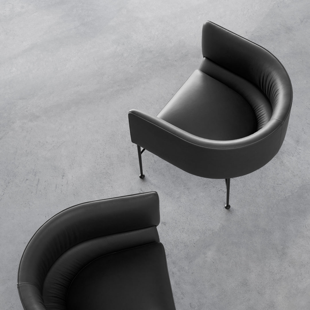 Black curved lounge chairs featuring a smooth leather texture and sleek metal legs against a grey background.