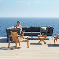 Coastal outdoor seating set featuring navy cushions, light wood accents, and minimalist design against a blue sea backdrop.