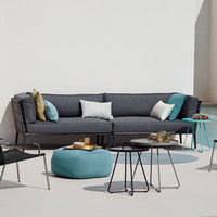 Modern outdoor sectional sofa in charcoal gray with turquoise and white accent pillows, surrounded by sleek black and aqua tables.