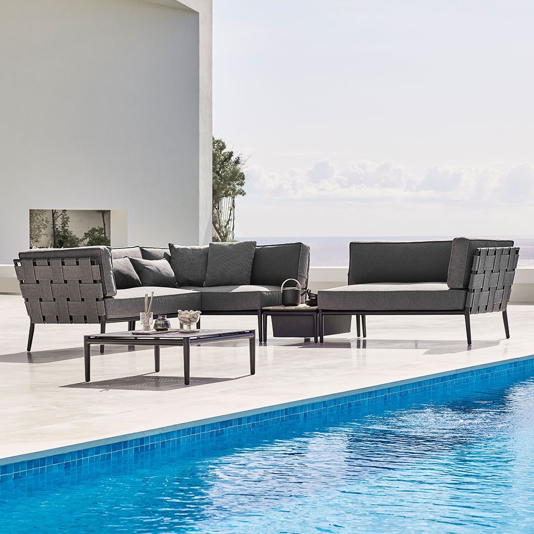 Modern outdoor sofa set in gray with tufted cushions, paired with a sleek black coffee table, near a blue pool.
