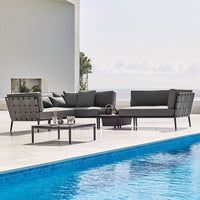 Modern outdoor sofa set in gray with tufted cushions, paired with a sleek black coffee table, near a blue pool.