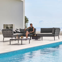 Modern outdoor seating set in sleek gray tones with textured cushions, paired with a minimalist black coffee table by a pool.
