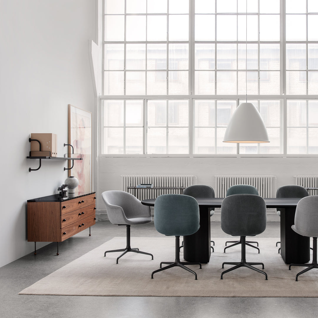 Modern meeting room with gray and teal chairs, wooden accents, and a light gray rug against a bright, airy backdrop.