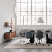Modern meeting room with gray and teal chairs, wooden accents, and a light gray rug against a bright, airy backdrop.
