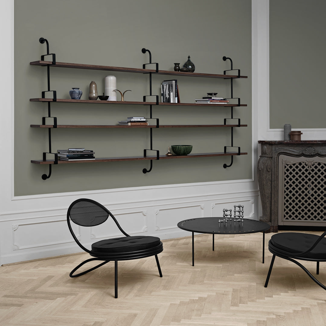 Modern black shelves with wooden accents against a soft green wall, paired with a black chair and coffee table.