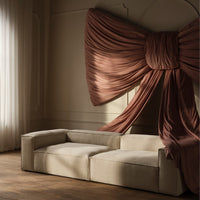 Beige sofa with smooth texture contrasted by flowing, rich brown drapery in an elegant, modern setting.