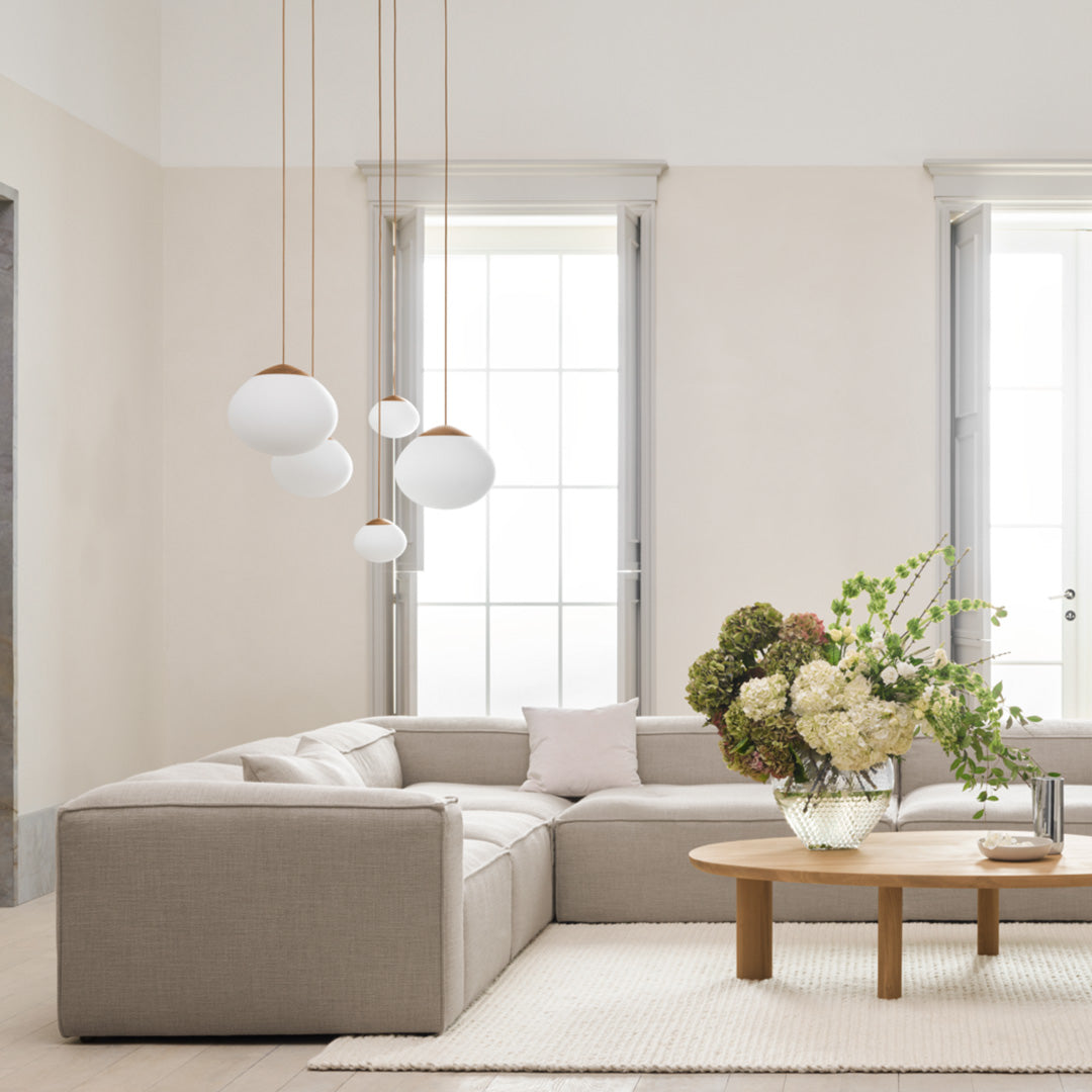 Modern beige sectional sofa with soft white and wood accents, paired with a round coffee table and lush floral arrangement.