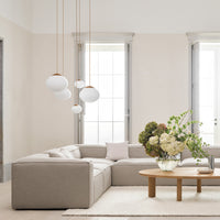 Modern beige sectional sofa with soft white and wood accents, paired with a round coffee table and lush floral arrangement.