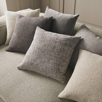 Assorted decorative pillows in soft greys, taupes, and textured patterns, arranged on a plush green sofa.