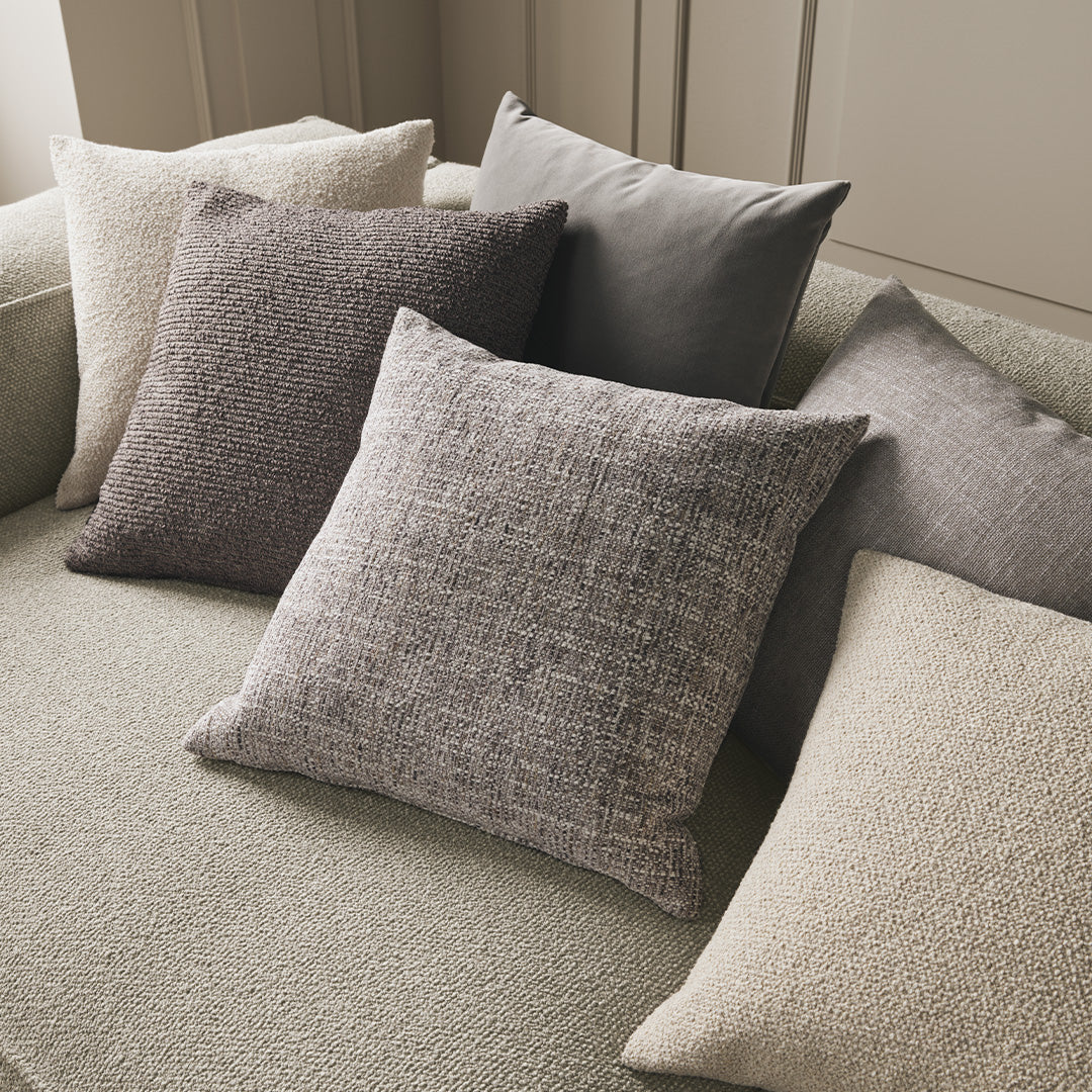 Assorted throw pillows in soft gray, beige, and textured patterns on a neutral green sofa. Perfect for modern decor.